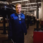 Mechanic standing with tool in his hand in front of a vehicle undergoing repairs