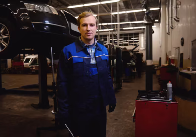 Mechanic standing with tool in his hand in front of a vehicle undergoing repairs
